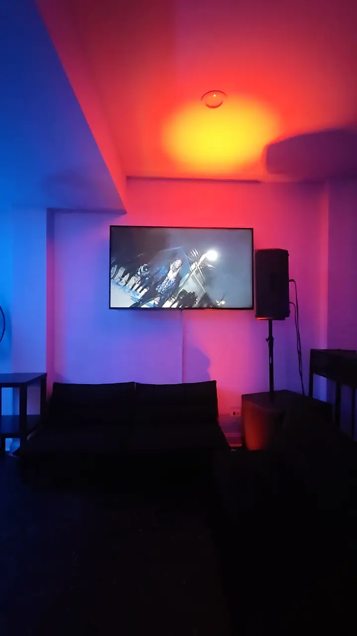 A sofa beneath a wall screen as the ceiling light shifts from amber to green.