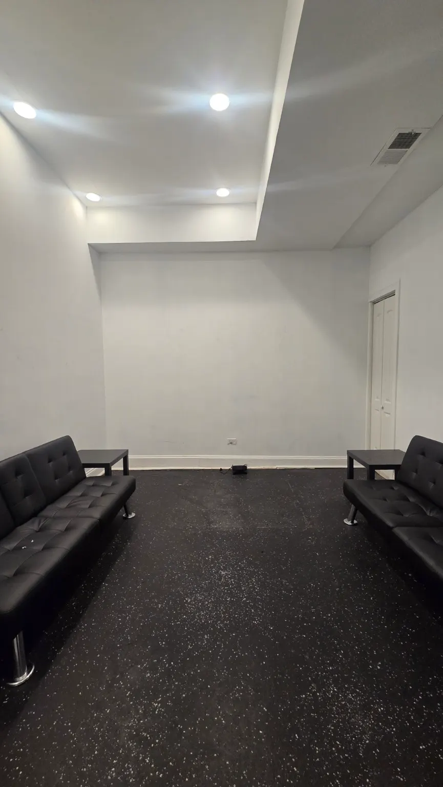 A private side room with black tufted sofas facing each other across a dark speckled floor.