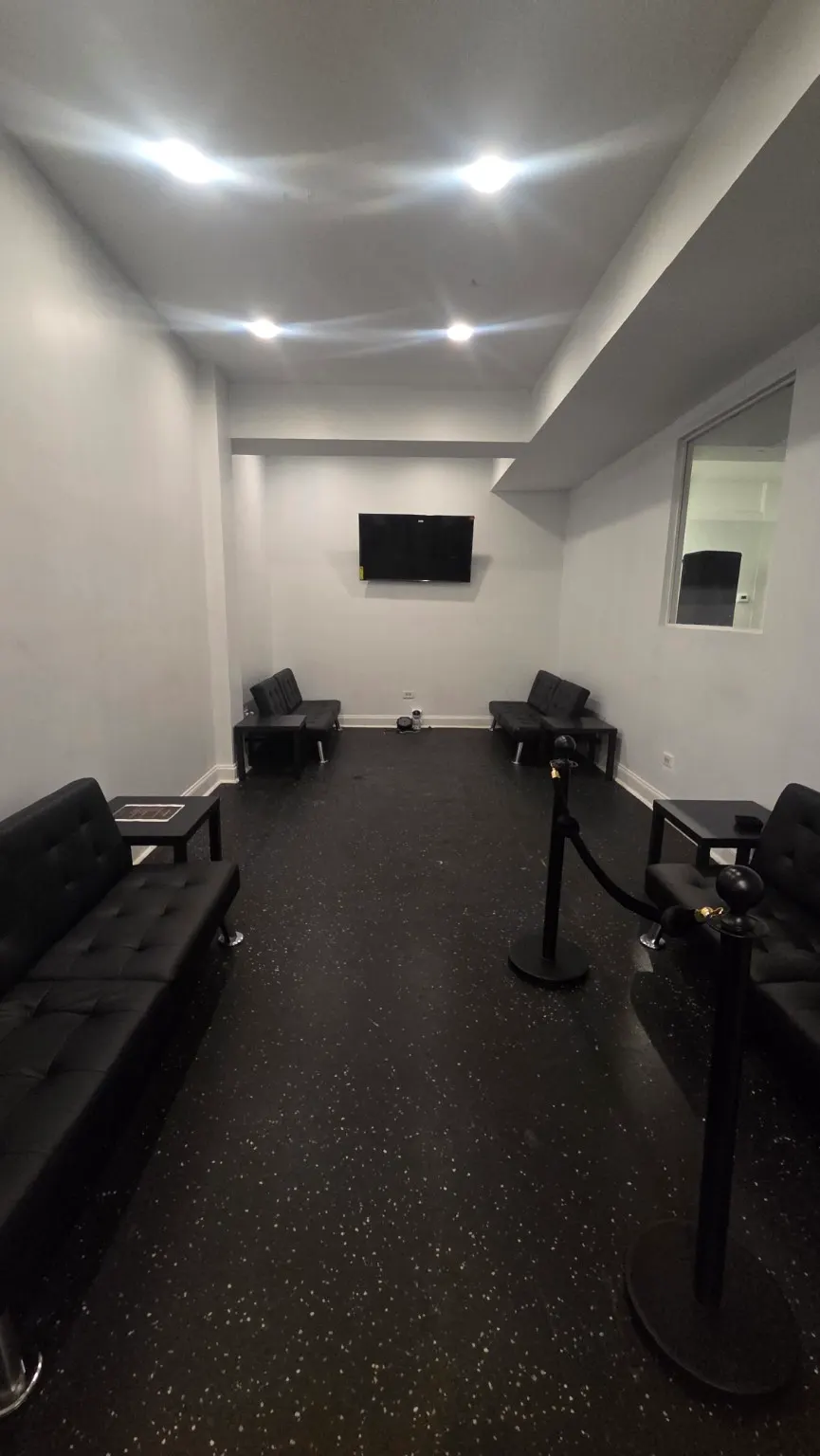 A long private room with black tufted sofas, side tables, velvet rope and a wall screen.